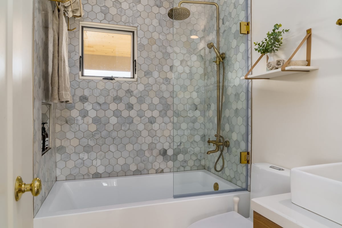 Modern remodeled bathroom with shower tub, hexagonal tile and gold fixtures
